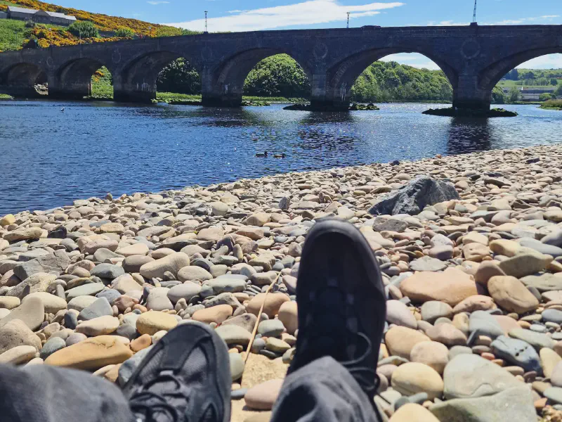 Wanderschuhe am Kiesstrand vor der alten Brücke