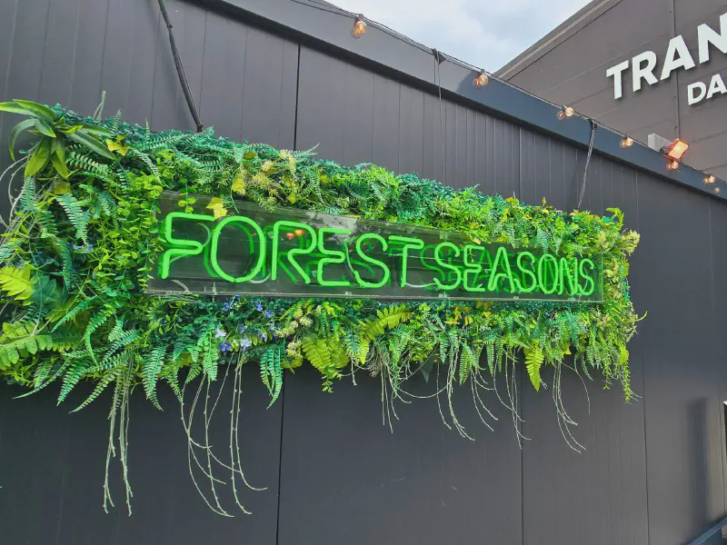 FOREST SEASONS sign in front of a sea of green leaves