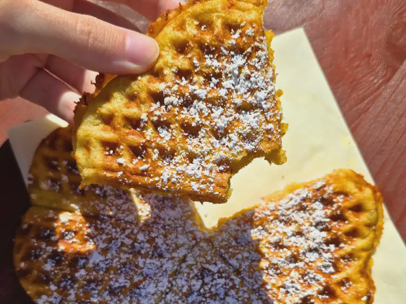 Hand hält eine Kürbiswaffel mit Puderzucker